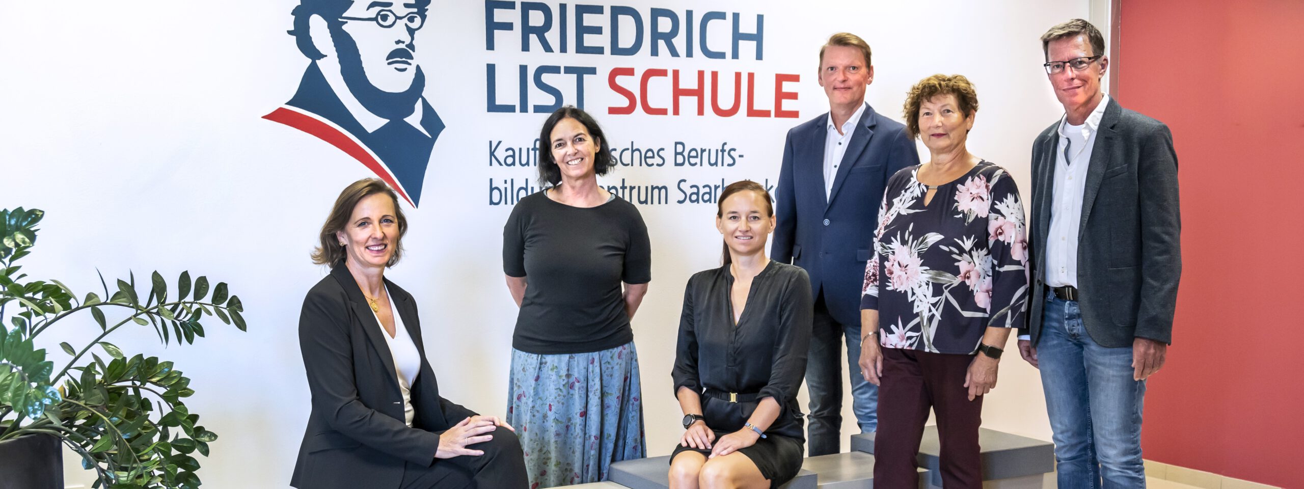 Vertreter des Fördervereins posieren vor dem Friedrich-List-Schule Logo